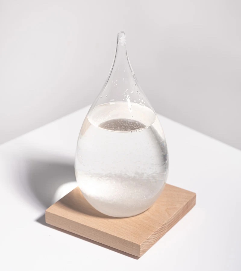 Storm glass en forme de goutte posé sur un socle en bois