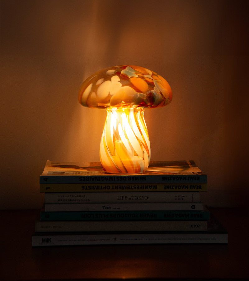 Lampe champignon en verre soufflé allumée, posée sur une pile de livres