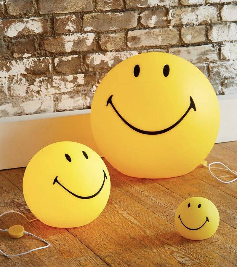 Trois lampes Smiley jaunes de tailles différentes posées sur un parquet