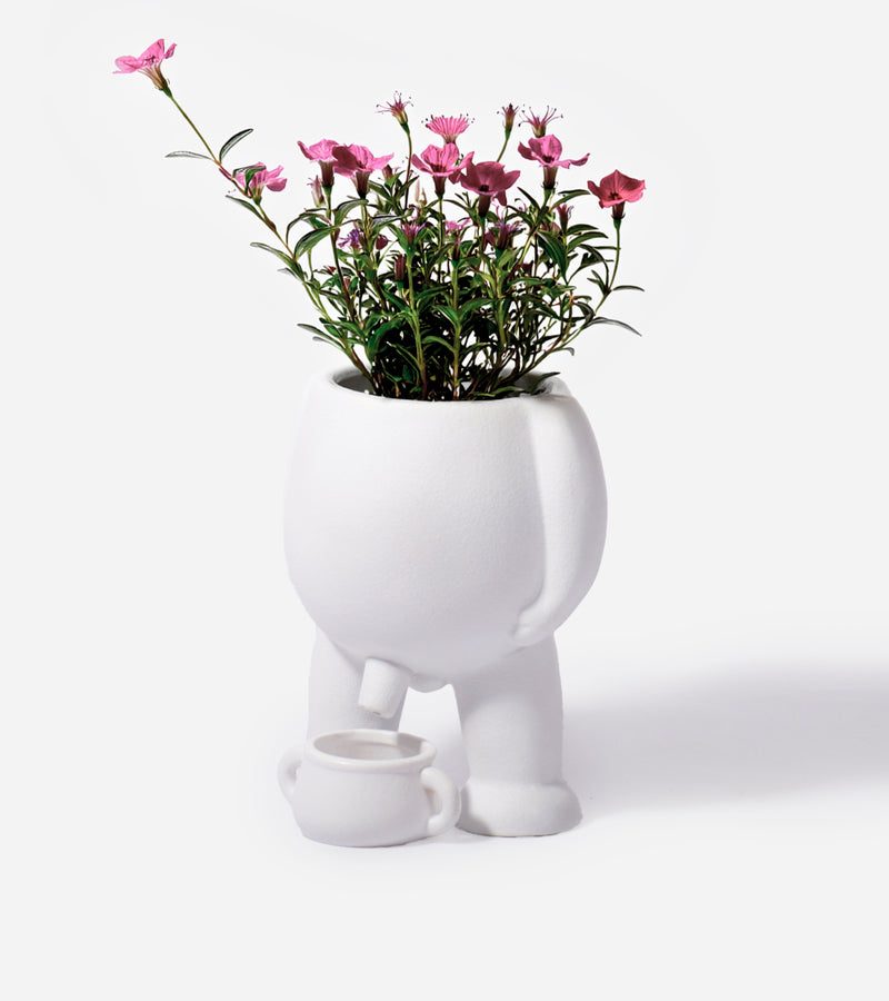 Pot de fleurs blanc en forme de personnage qui fait pipi dans un petit pot de chambre