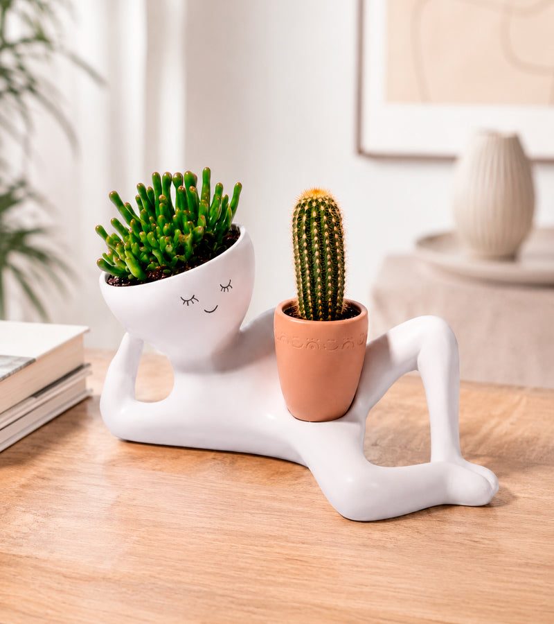 Pot de fleurs en forme de bonhomme blanc allongé avec une succulente et un cactus