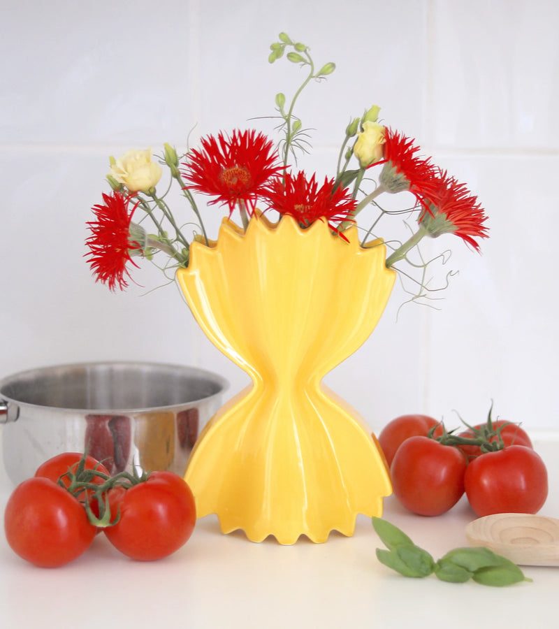 Vase jaune en céramique en forme de pâte farfalle avec des fleurs rouges