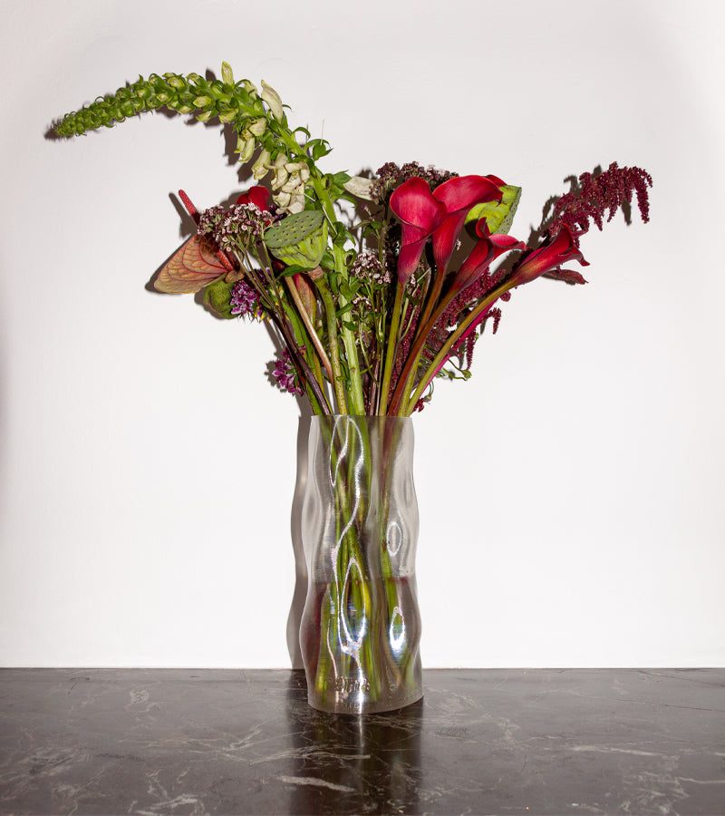 Vase Magma transparent aux formes ondulées avec un bouquet de fleurs rouges