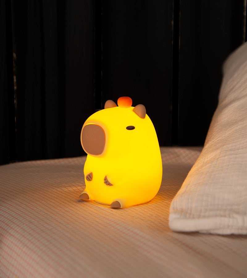 Veilleuse capybara jaune allumée posée sur un lit