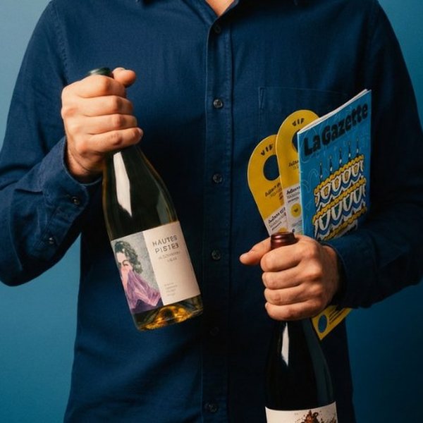 Homme tenant deux bouteilles de vin et la gazette mensuelle du Petit Ballon