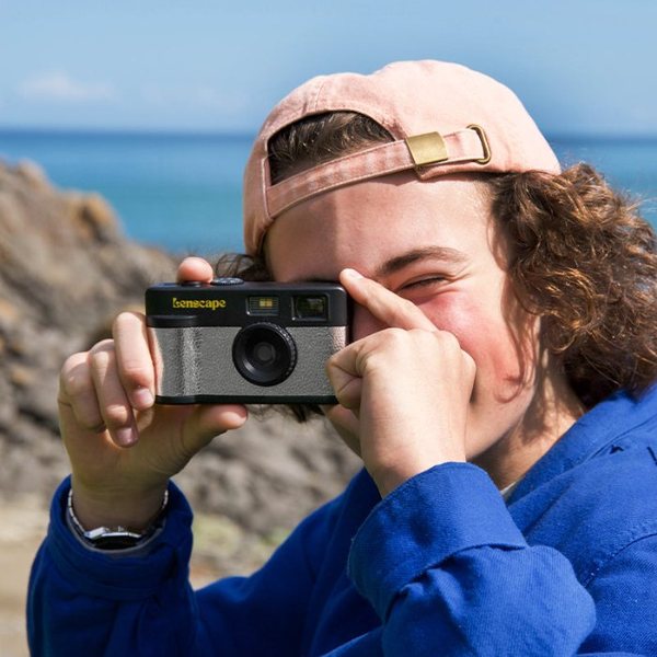 Jeune homme prenant une photo avec un appareil photo numérique compact rétro au bord de la mer