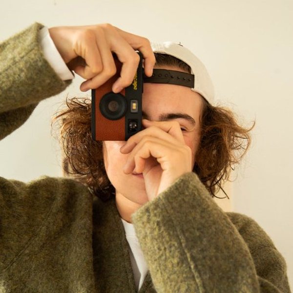 Jeune homme à casquette prenant une photo avec un petit appareil numérique rétro marron