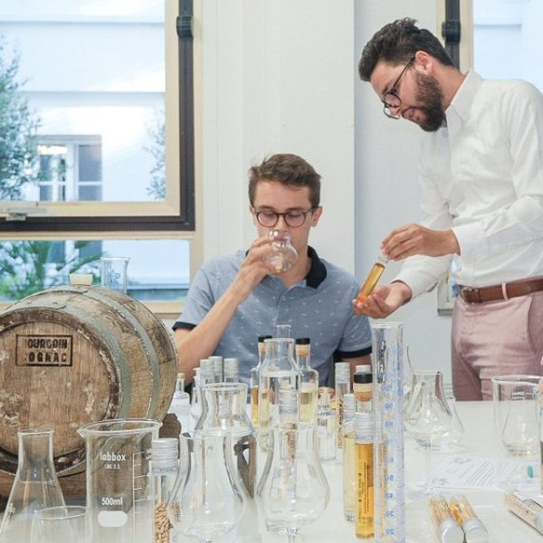 Deux hommes assemblant un whisky avec des éprouvettes et des verres dans un atelier lumineux