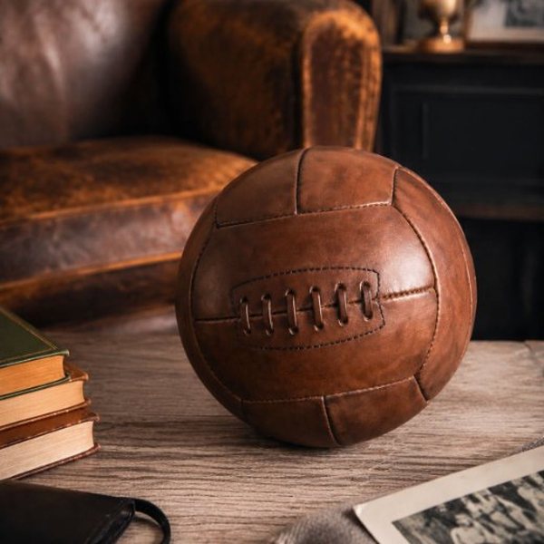 Ballon de football ancien en cuir marron posé sur une table en bois
