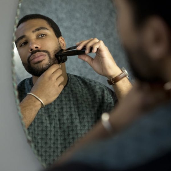 Homme se taillant la barbe avec un bavoir à barbe fixé au miroir