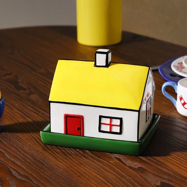 Beurrier en forme de petite maison jaune et blanche posé sur une table en bois
