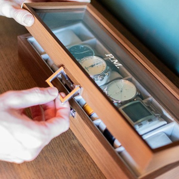 Main ouvrant une boîte à montres en bois à couvercle vitré contenant plusieurs montres