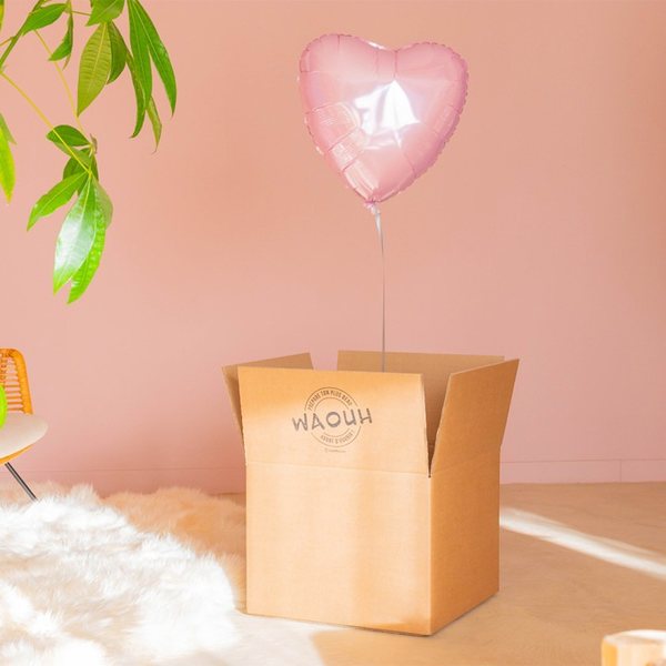 Carton ouvert d'où s'élève un ballon cœur rose gonflé à l'hélium