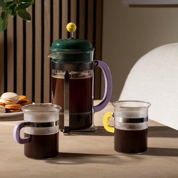 Cafetière à piston verte MoMA x Bodum remplie de café à côté de deux tasses sur une table