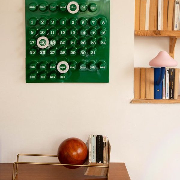 Calendrier perpétuel Ring a Date vert avec anneaux blancs accroché au mur au-dessus d'un bureau