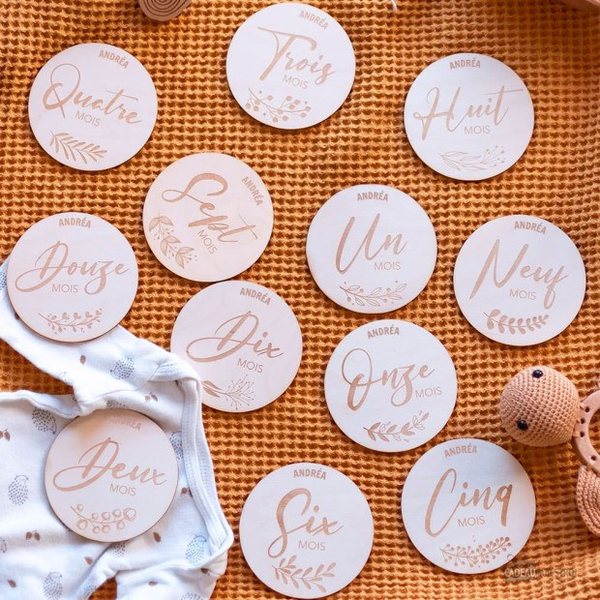 Douze cartes rondes en bois gravées des mois de bébé de Un à Douze, étalées sur un plaid orange