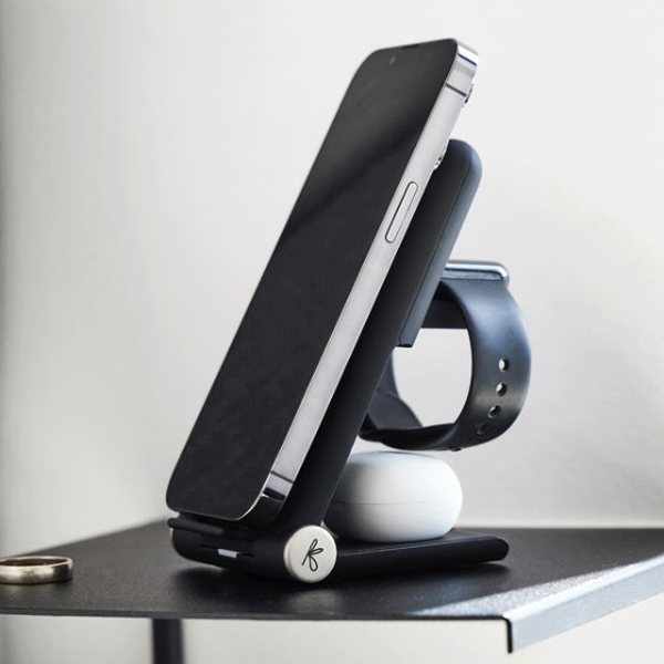 Station de charge noire rechargeant un smartphone, une montre et des écouteurs sur un bureau