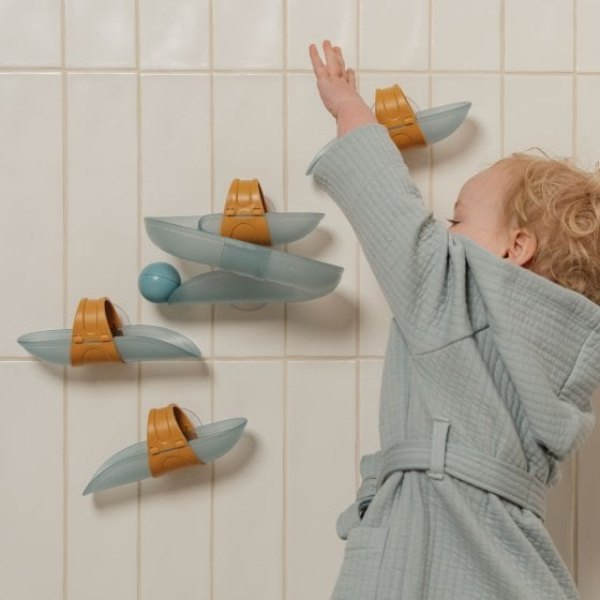 Enfant jouant avec un circuit de toboggans à balles fixé au carrelage de la baignoire