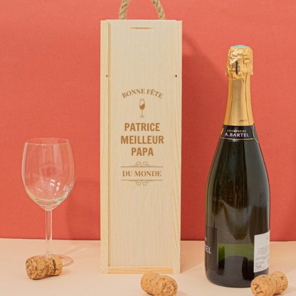 Coffret en bois gravé d'un message personnalisé à côté d'une bouteille de champagne et d'une flûte sur fond rouge