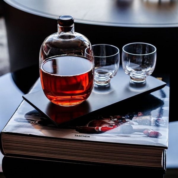 Carafe à whisky avec bouchon et deux verres en cristal posés sur un plateau noir au-dessus de livres