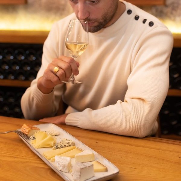 Homme goûtant un verre de vin blanc devant une planche de fromages dans une cave voûtée