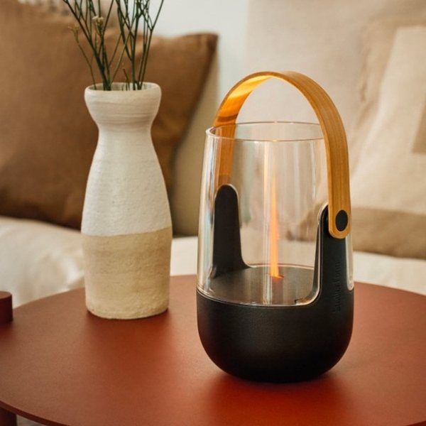Diffuseur Stadler Form noir à anse dorée avec une flamme lumineuse ambrée, posé à côté d'un vase