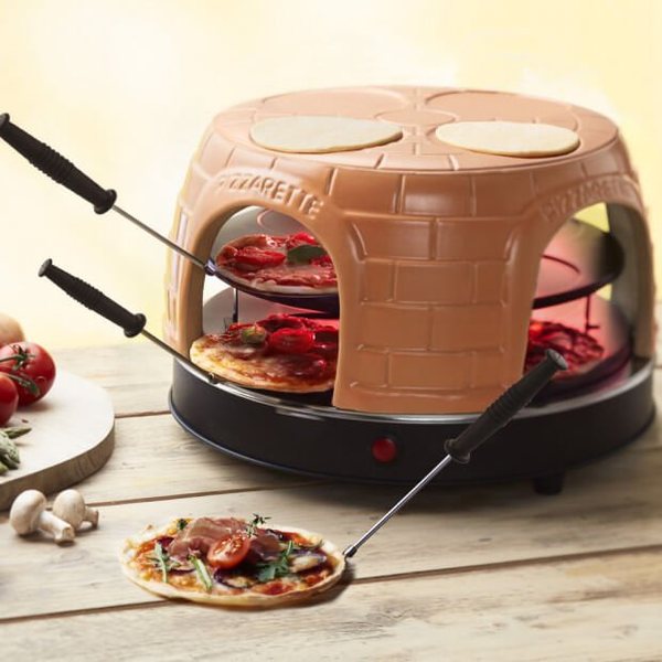 Four Pizzarette en terre cuite avec mini pizzas qui cuisent et spatules en bois, sur une table