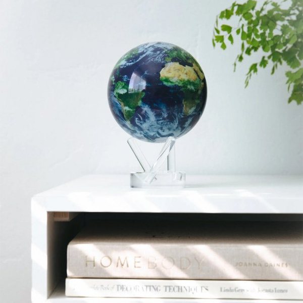 Globe terrestre Mova avec nuages tournant sur un socle transparent, posé sur une étagère blanche