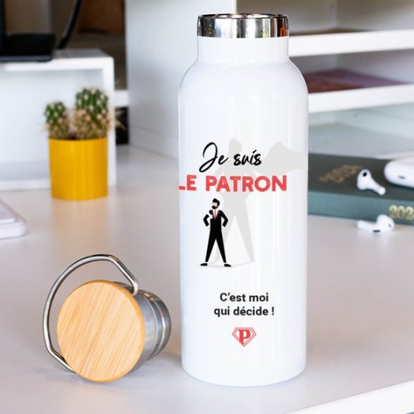 Gourde isotherme blanche « Je suis le patron » avec bouchon en bambou posée sur un bureau