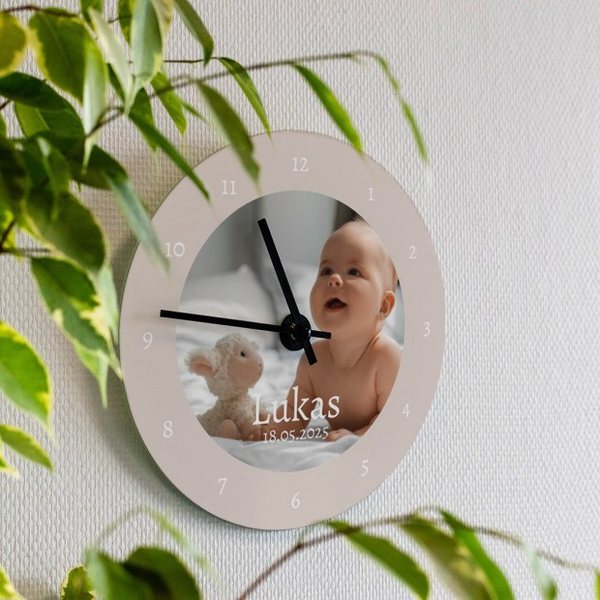 Horloge murale ronde avec la photo d'un bébé et le prénom Lukas, accrochée près d'une plante