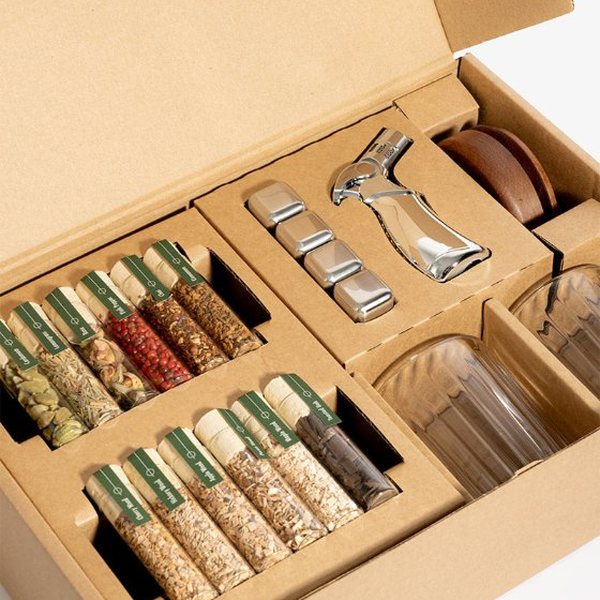 Coffret de fumage pour whisky ouvert avec tubes de bois, épices, chalumeau et deux verres