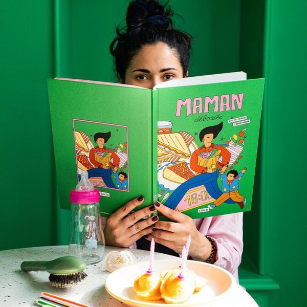 Femme lisant le livre de cuisine illustré Maman débordée à une table avec un biberon
