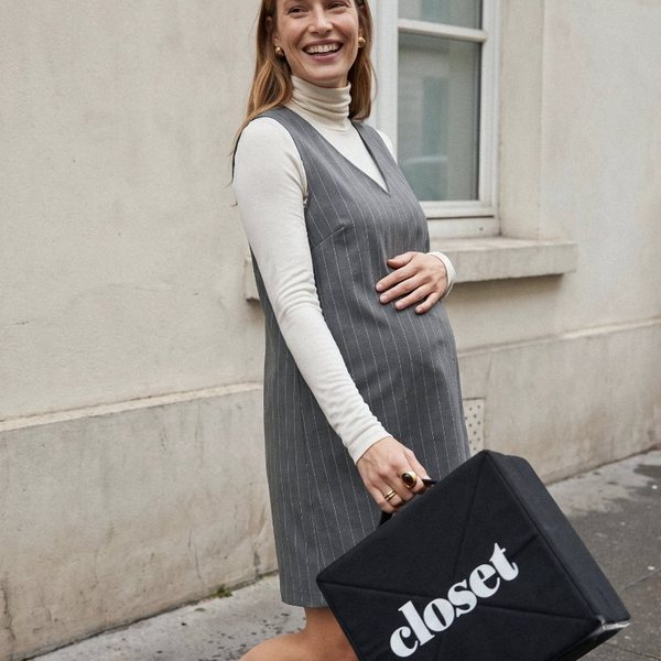Femme enceinte souriante en robe chasuble grise marchant dans la rue avec un sac Le Closet