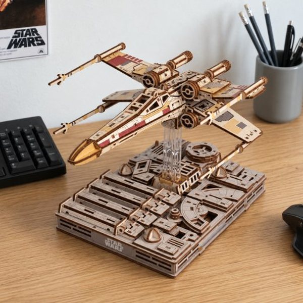Maquette en bois d'un X-Wing de Star Wars posée sur un socle à côté d'un clavier