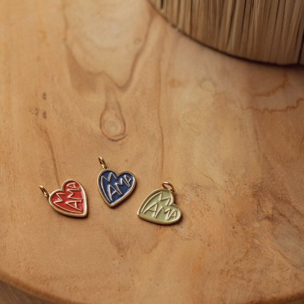 Trois médaillons en forme de cœur émaillés rouge, bleu foncé et sauge gravés Mama, posés sur du bois