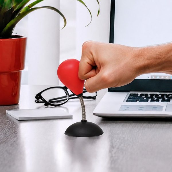 Main qui frappe un mini punching-ball rouge fixé sur un bureau à côté d'un ordinateur portable