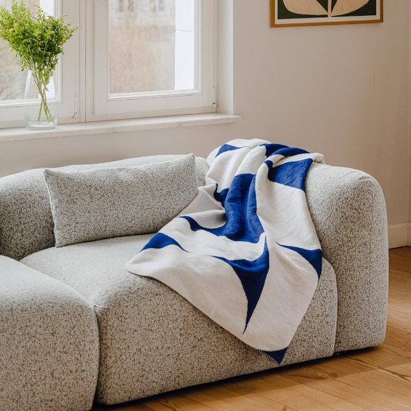 Plaid bleu et beige à motifs géométriques posé sur un canapé bouclette gris