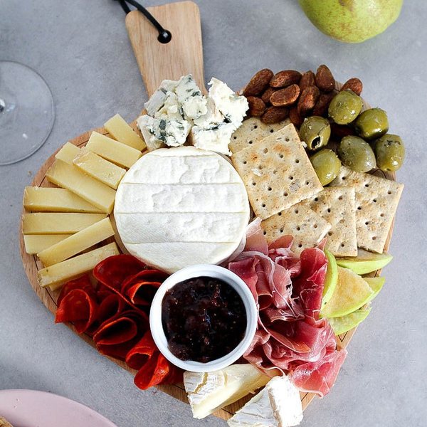 Planche en bois garnie de fromages, charcuterie, crackers, olives et confiture