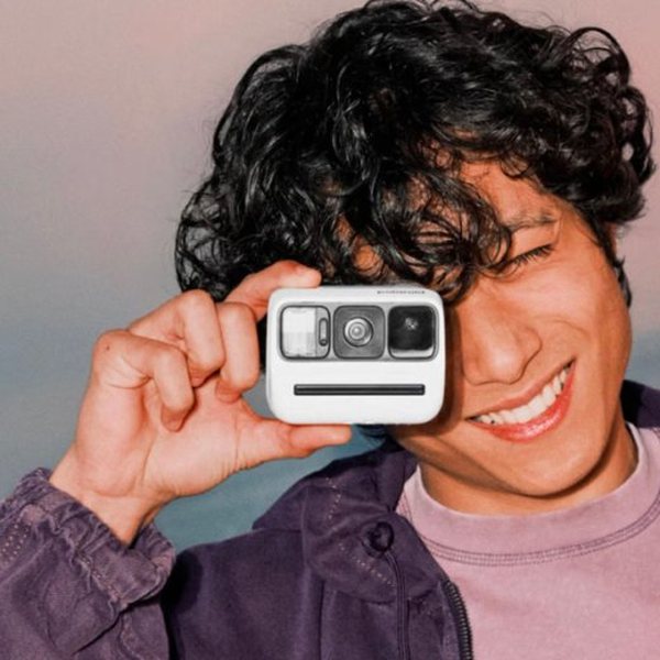 Jeune homme souriant prenant une photo avec un appareil Polaroid Go blanc