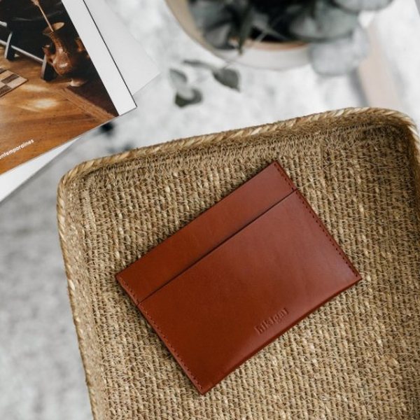Porte-cartes en cuir cognac posé dans une corbeille en osier sur une table