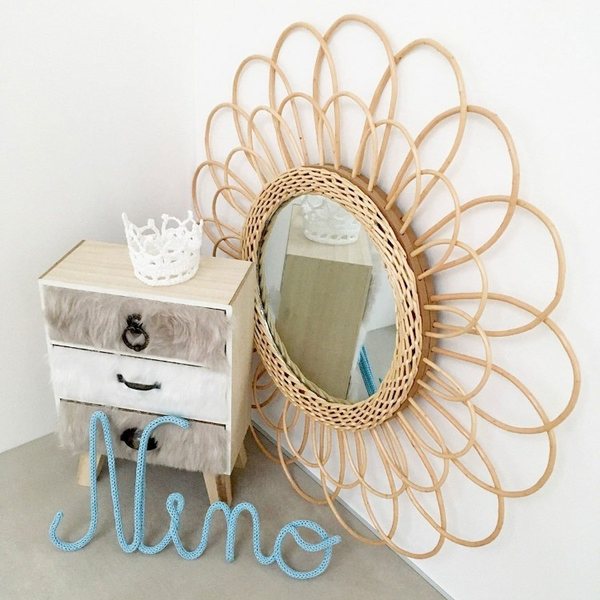 Prénom Nino en tricotin bleu ciel posé devant une commode et un miroir soleil en rotin