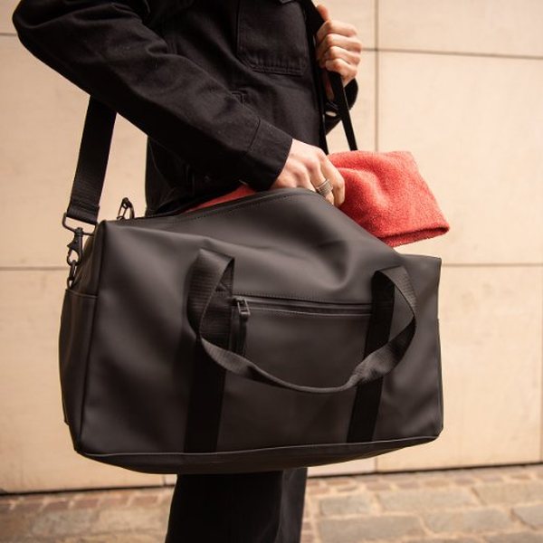 Personne sortant un vêtement d'un sac de sport Rains noir imperméable