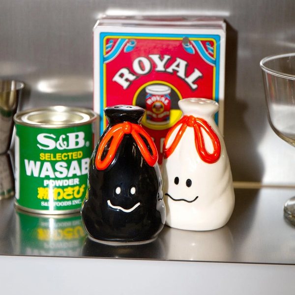 Salière blanche et poivrière noire en céramique en forme de sacs-poubelle à lien orange, à côté de boîtes de conserve