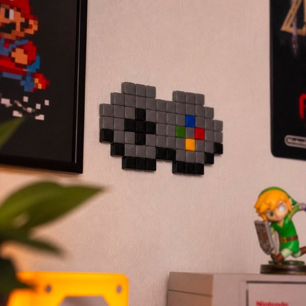 Mosaïque pixel en forme de manette de jeu rétro posée sur une étagère avec des figurines