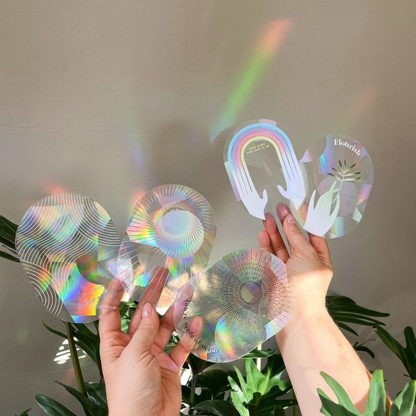 Mains qui tiennent des stickers suncatcher projetant des arcs-en-ciel près d'une fenêtre