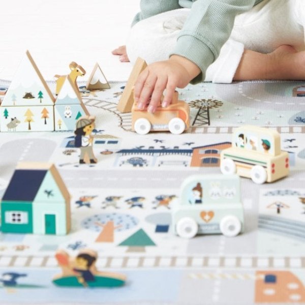 Enfant jouant sur un tapis circuit enneigé avec des véhicules et des maisons en bois
